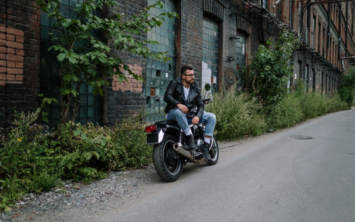 Man in a leather jacket sitting casually on a motorcycle in an urban setting