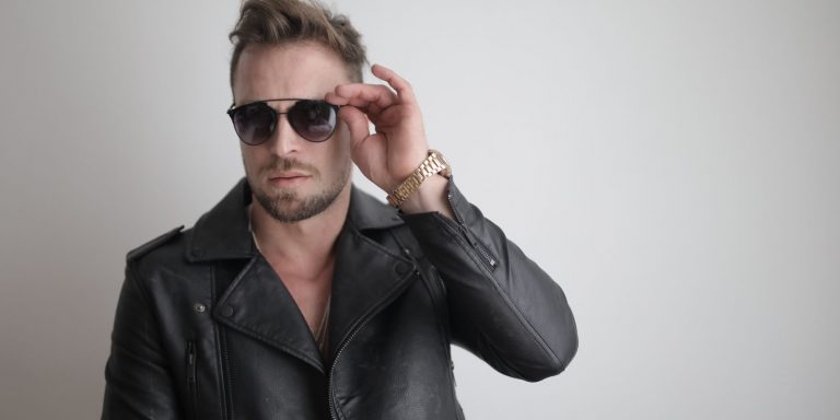 Fashionable man in a black leather jacket and sunglasses posing indoors