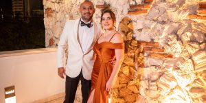 Stylish couple in formal evening attire posing together against an illuminated stone wall
