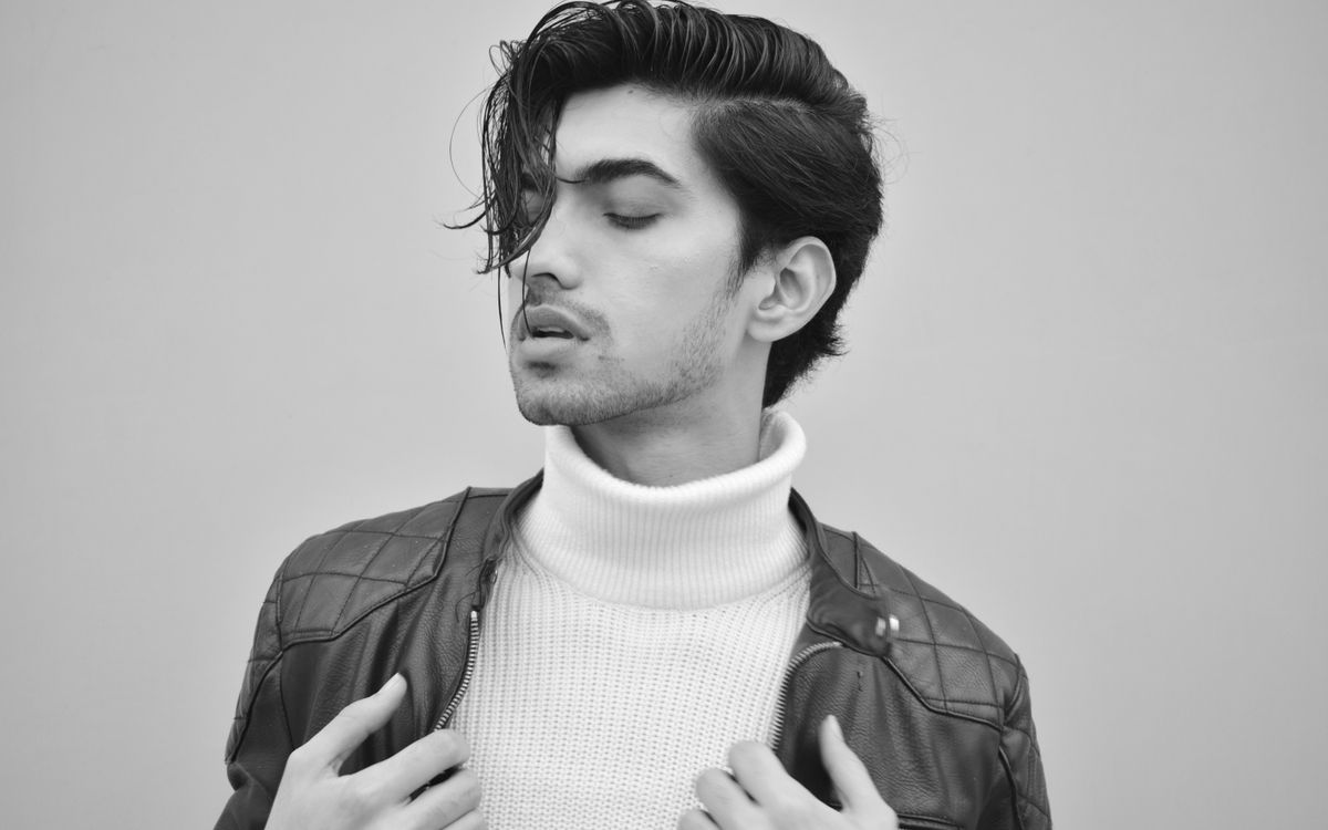 Black and white portrait of a person posing in a stylish, sharply tailored outfit