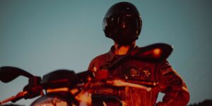 A motorcyclist in helmet and leather jacket poses beside a bike at twilight