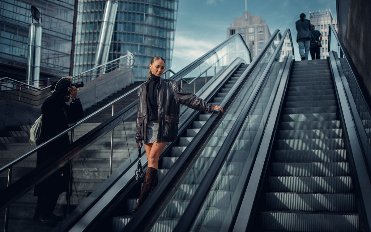 A stylish woman posing on an urban escalator in a leather jacket for a modern fashion shoot