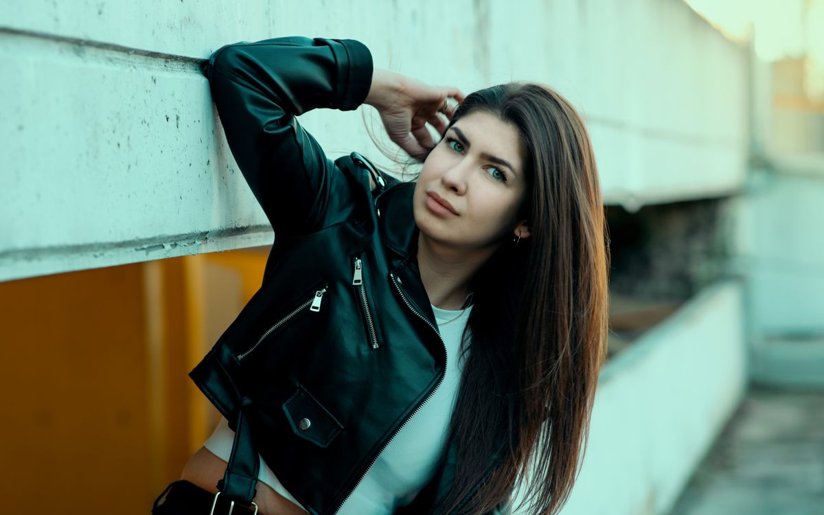 A stylish woman in a black leather jacket poses confidently in an urban setting