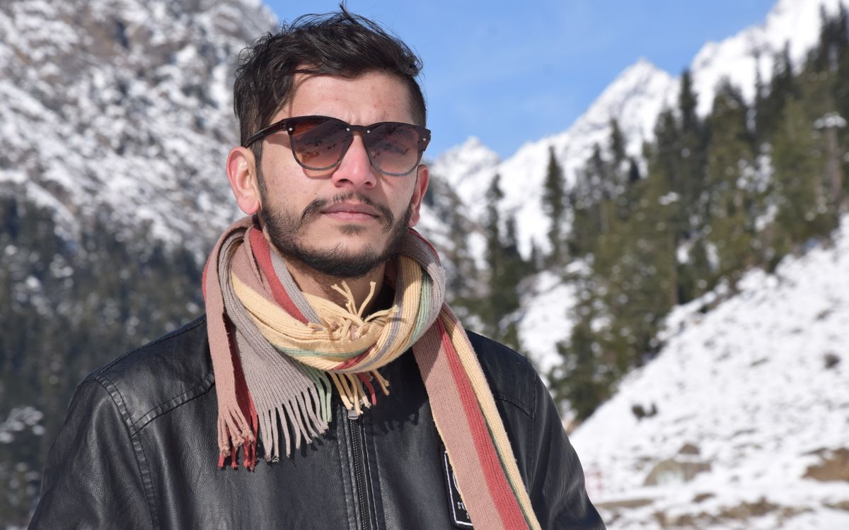 A man in a scarf against a backdrop of snowy mountains on a cold clear day
