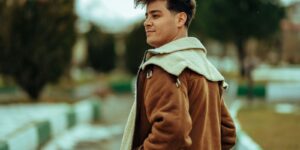 A fashionable young man in a brown jacket posing outdoors, showing the texture of the leather