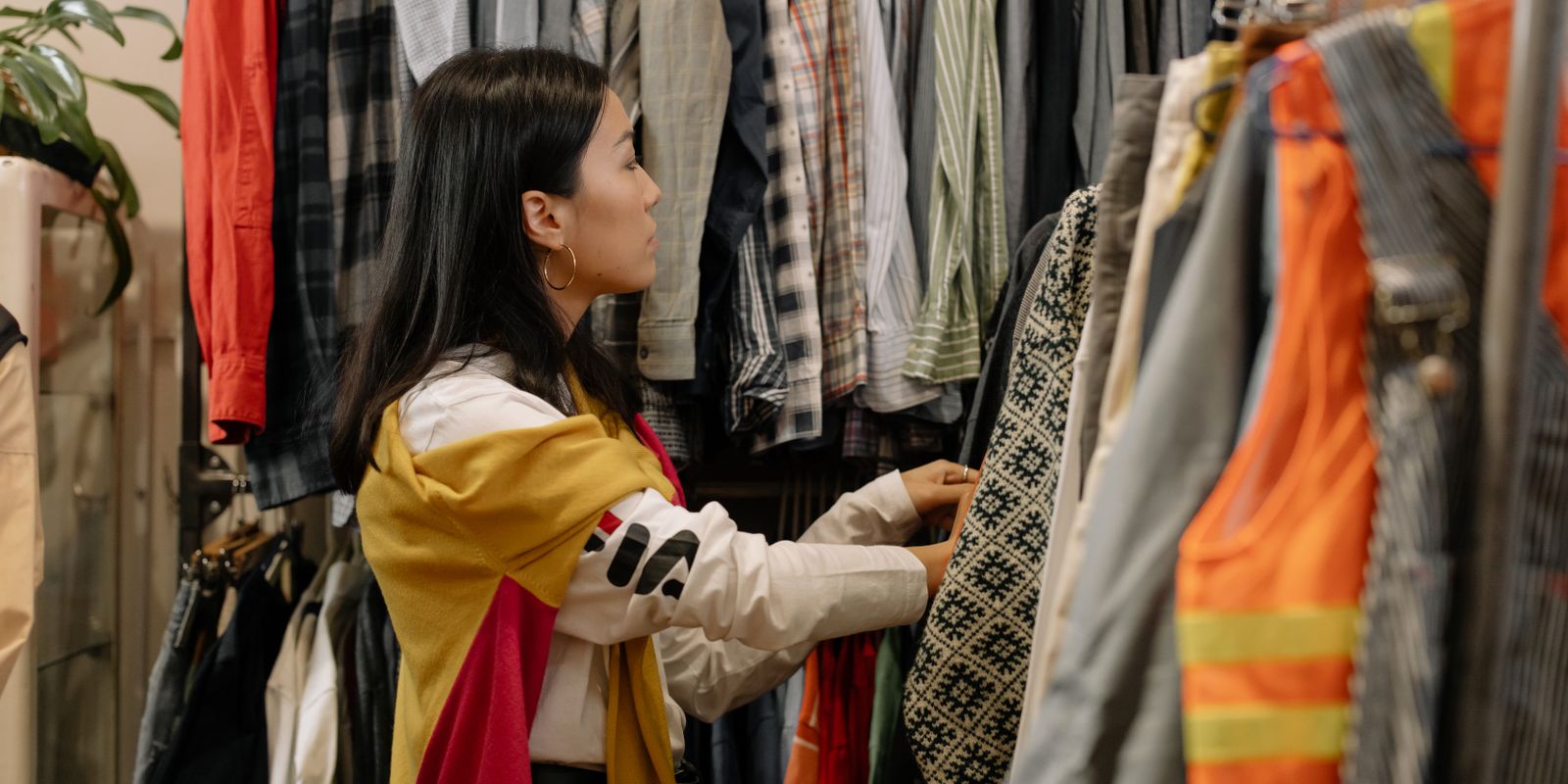 A young woman browsing a rack of clothing in a vintage store full of colourful outfits