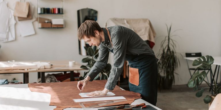 A craftsman designs and cuts leather in a sunlit workshop, showcasing handmade artistry