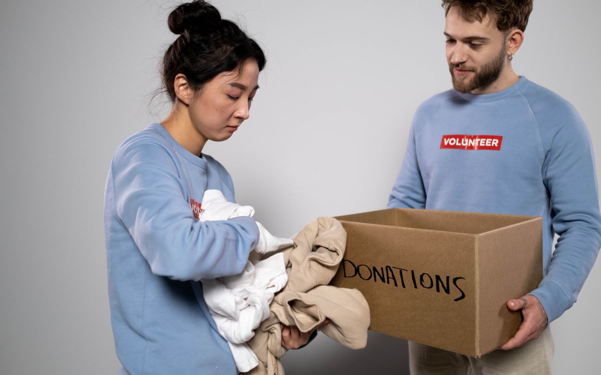 Two volunteers organizing clothes into a donation box, showcasing community service and generosity