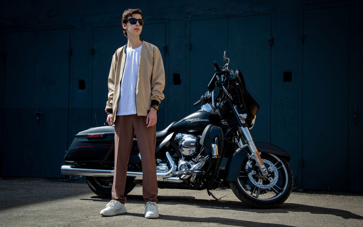 A man in casual style posing with a motorcycle outdoors