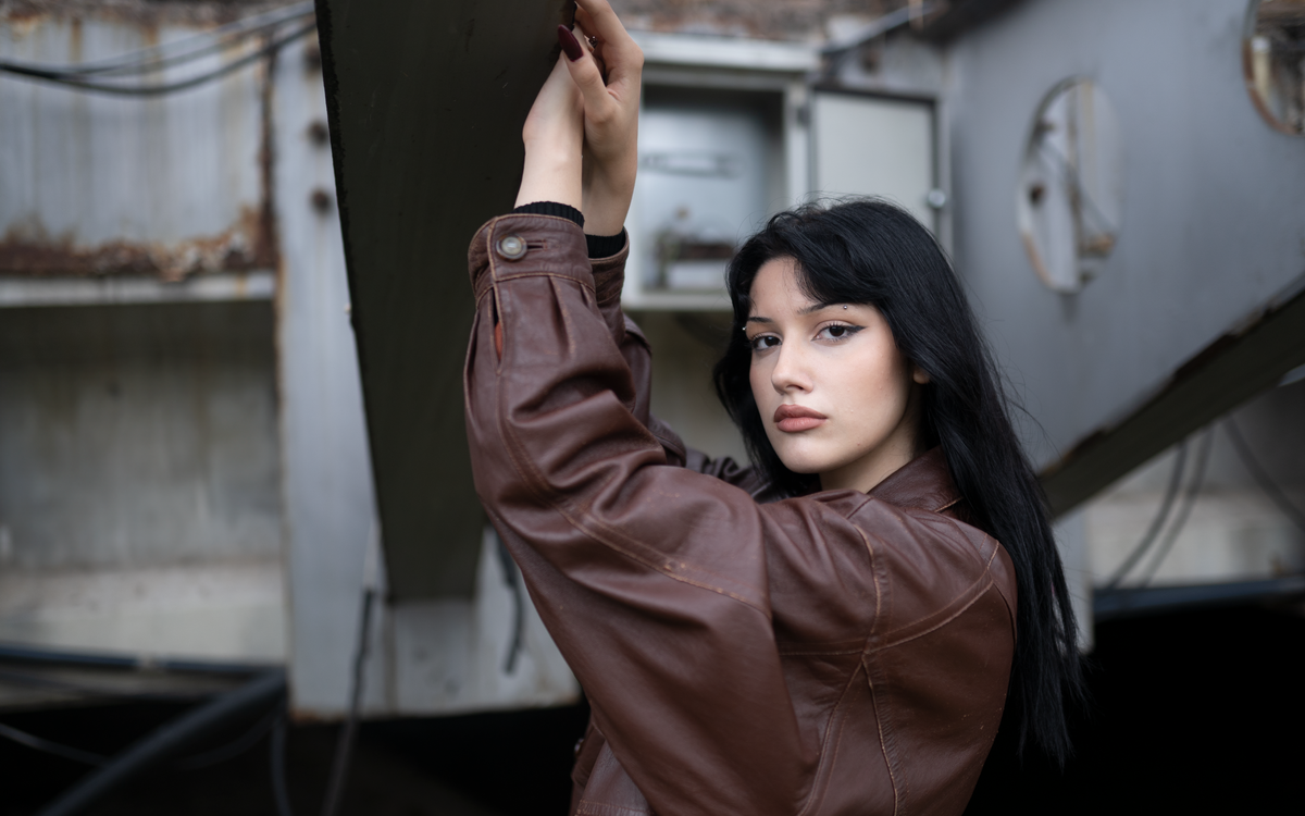 A young woman wearing a brown leather jacket with a confident expression