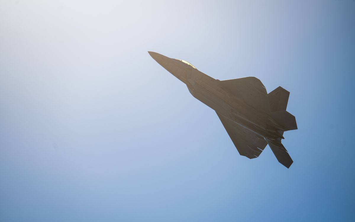 Silhouetted fighter jet flying against a clear blue sky