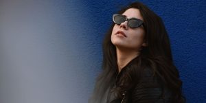 A stylish woman in a leather jacket posing against a vibrant blue wall