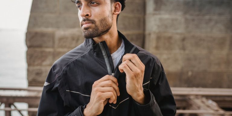 A young man zipping up a leather jacket on a city street