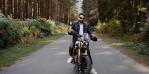 A rider in a black leather jacket on a motorcycle along a scenic forest road