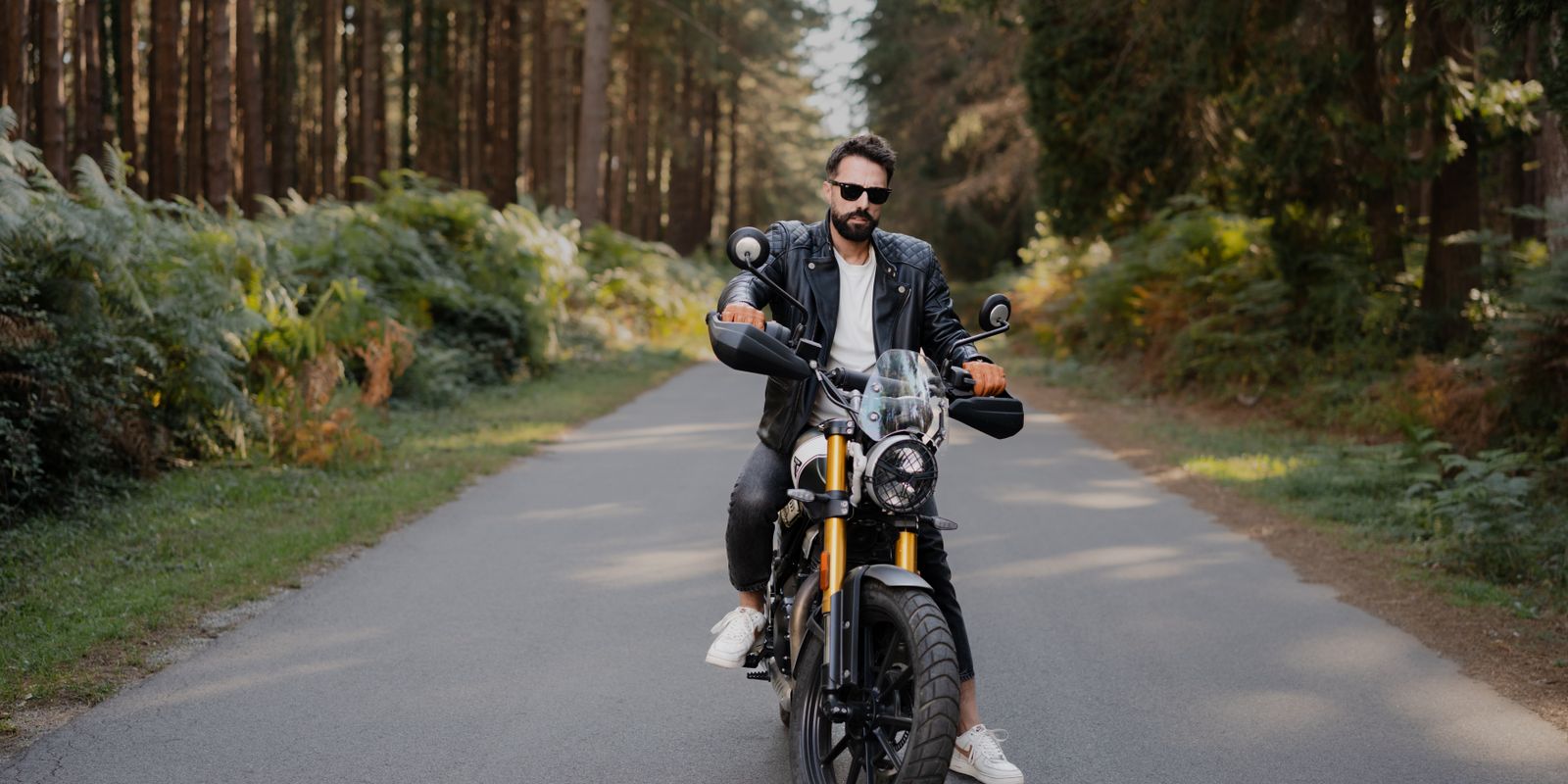 A rider in a black leather jacket on a motorcycle along a scenic forest road