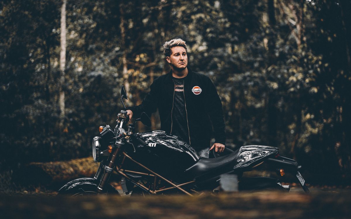 A man standing beside a black vintage motorcycle among trees