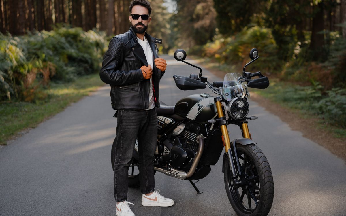 A stylish man posing with a motorcycle on an open road