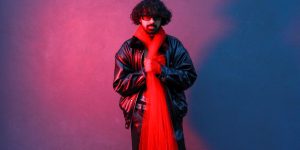 A stylish man in a red leather jacket posing against a dramatic red and blue backdrop