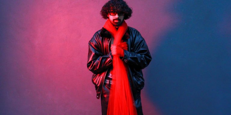 A stylish man in a red leather jacket posing against a dramatic red and blue backdrop