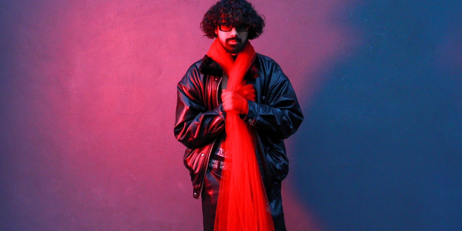 A stylish man in a red leather jacket posing against a dramatic red and blue backdrop