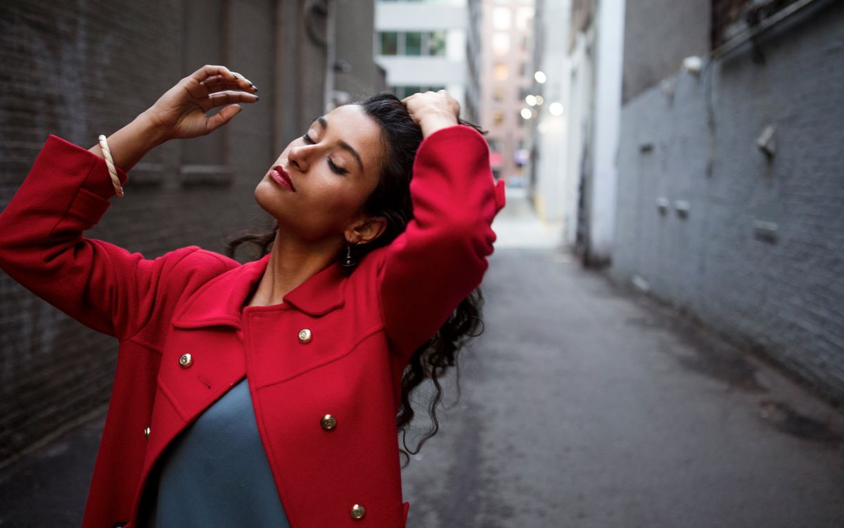 A stylish person in a red jacket posing in an urban street setting