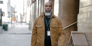 A man with a beard walking confidently through the city in a brown leather overshirt