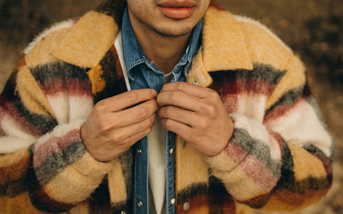 A man adjusting the collar of his overshirt outdoors on a crisp autumn day